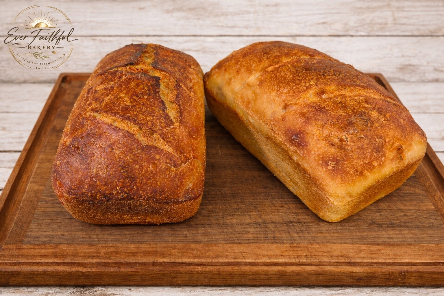 A pair of golden sourdough sandwich loaves on a wooden board